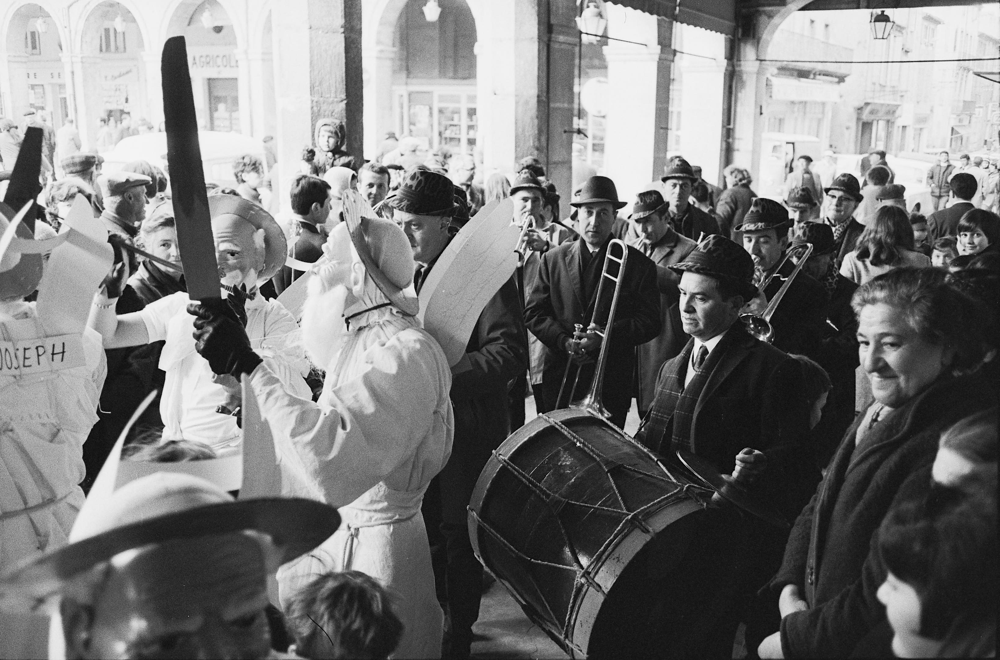 Sortie d'une bande de "fécos" avec la fanfare municipale sous les arcades de la place de la République, Limoux (Aude), 25 février 1968 (cliché Claudie Marcel-Dubois, Ph.2011.0015.059)